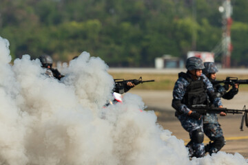 Naklejka premium Smoke from smoke bomb and military personnel walking on the road.Group of military men holding gun.Soldiers in military uniform with machine guns training on the battlefield.