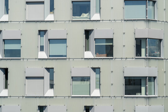 View of the modern building facade with symmetrical windows reflecting the sky, creating a rhythmic pattern of light and shadow, Oslo, Oslo, Norway.
