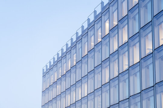 View of a modern building with symmetrical glass windows reflecting the soft blue sky, creating a serene and minimalist urban scene, Oslo, Norway.