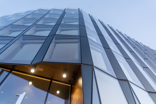 View of the geometric patterns of a modern building's glass facade reflect the sky, with the number '1' prominently displayed at the entrance, Oslo, Norway.