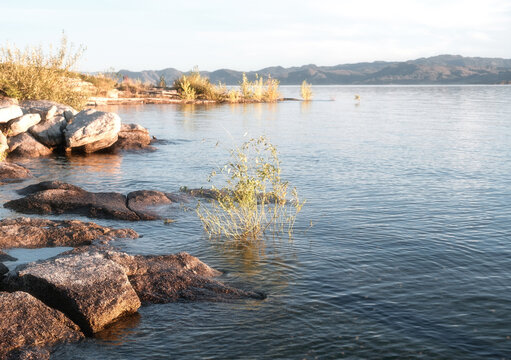 Rocky shore of Bukhtarma reservoir in East Kazakhstan at sunset with calm water and mountains in the background. landscape suitable for travel marketing, environmental topics, and summer vacation