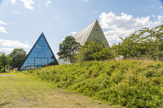 View of striking triangular buildings rise from a verdant hill under a bright, cloud-strewn sky, blending modern architecture with the natural landscape, Oslo, Norway.