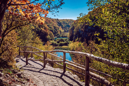 View of a stone path with a wooden fence overlooking the turquoise lakes surrounded by autumn foliage, Plitvicka Jezera, Lika-Senj County, Croatia.