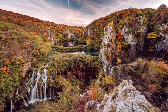 View of cascading waterfalls plunging into turquoise pools amidst vibrant autumn foliage, connected by wooden walkways, Plitvicka Jezera, Lika-Senj County, Croatia.