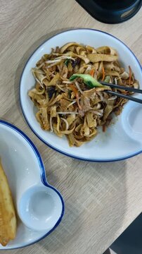 POV. Noodle plate with fried roll and chopstick, lunch break with visible legs as UGC, food blogger framing shot. 
