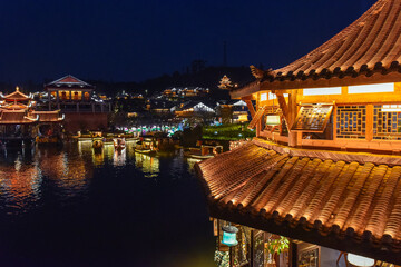 Obraz premium Night view of traditional stilt houses with glowing lanterns reflecting on the river in Moon Fields (Yueliangtian) scenic spot in Lizhuang Ancient Town, Yibin, Sichuan, China