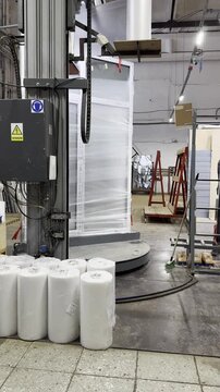 Industrial pallet wrapper machine wraps plastic film around cargo in warehouse. Automated packaging technology for efficient logistics and shipping in factory.