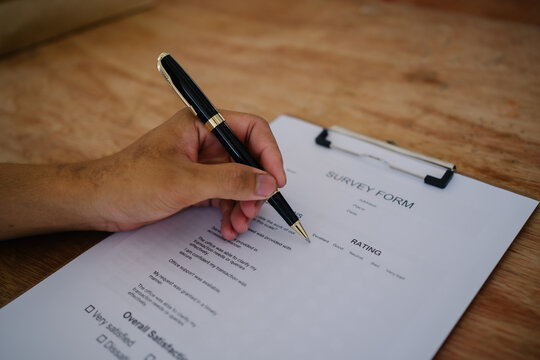 Hand filling out customer satisfaction survey form on clipboard with pen for business feedback and research