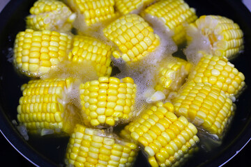Corn pieces boiling in hot water inside a pan.
