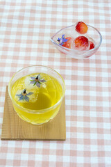 ギンガムチェックのテーブルクロスに置かれたボリジを浮かべた冷茶と冷凍されたサクランボ