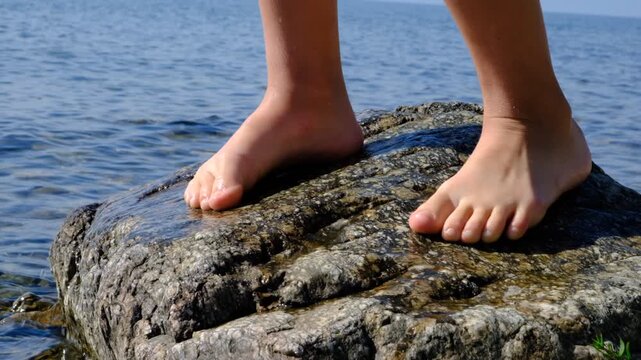 Teenager, barefoot child enjoying nature on the beach. Standing on boulder, natural massage for foot. Rocky shore