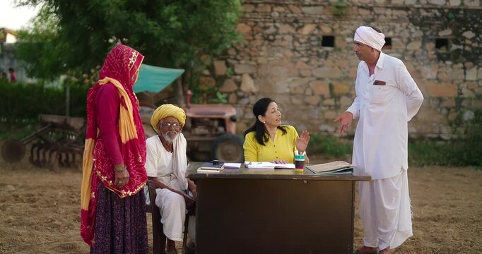 Indian worker sitting on chair do village visit field work talk with old aged male female issue staff look book file check report data speak share bank loan enquiry to man at rural area ground place