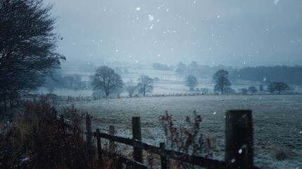 Winter landscape with snow gently falling across peaceful countryside field