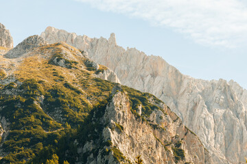 A dramatic landscape of the Julian Alps featuring rugged limestone peaks illuminated by warm golden hour light during a clear sunset. Stock photo background