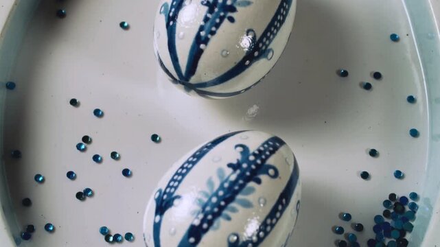 Two Blue and White Patterned Easter Eggs with Blue Glitter on Plate patterned eggs traditional