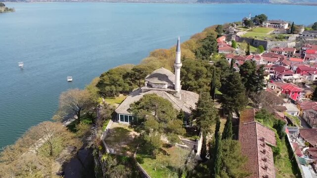 Drone footage starting with a close view of the Aslan Pasha Mosque on the cliffside and slowly pulling back to reveal the historic citadel of Ioannina Castle and the surrounding lake in Greece
