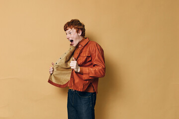 Man with surprised expression opening jacket in excitement, wearing orange shirt and dark jeans on...