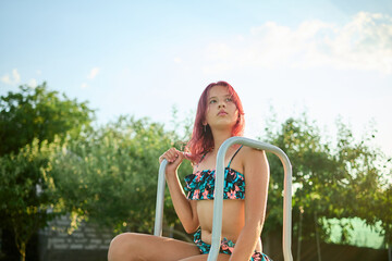 Teen girl relaxing at the edge of a pool in a colorful bikini while enjoying a sunny day outdoors