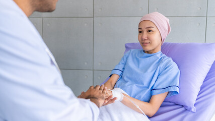 Obraz premium Asian woman cancer patient smiling and happy with health checkup result after listening to oncologist explanation while sitting on bed and looking at man doctor in lab coat in hospital ward.