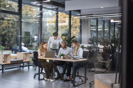 A modern office interior, featuring a blurred view of workers at desks, through a glass partition