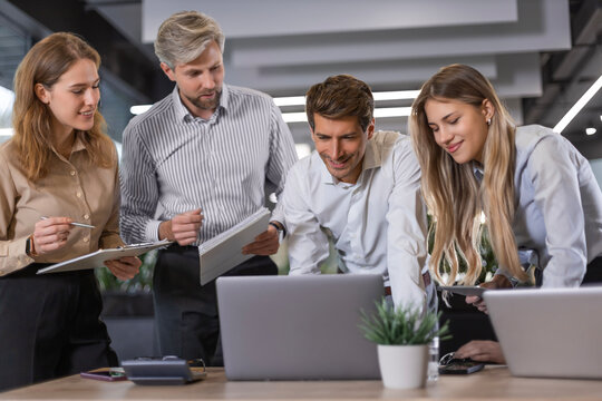 Business people discussing work together using a tablet and laptop taking notes in a modern office.