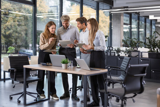 Business people discussing work together using a tablet and laptop taking notes in a modern office.