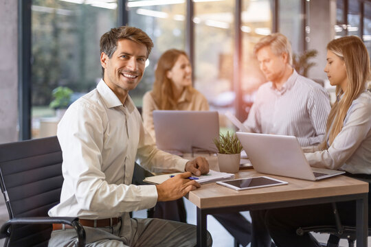 Handsome young businessman sitting confident in the office in front of his team.