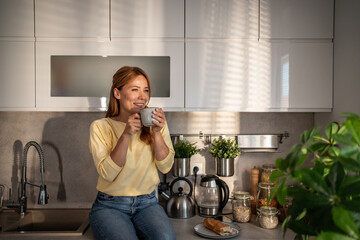 Woman enjoying morning coffee in contemporary kitchen basking in sunlight