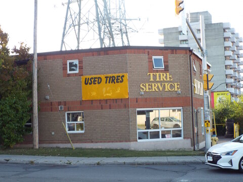 Ottawa, Ontario, Canada-July 18, 2025: A tan and red brick commercial building features prominent yellow "USED TIRES" and "TIRE SERVICE" signage at 1981 Bank St.

