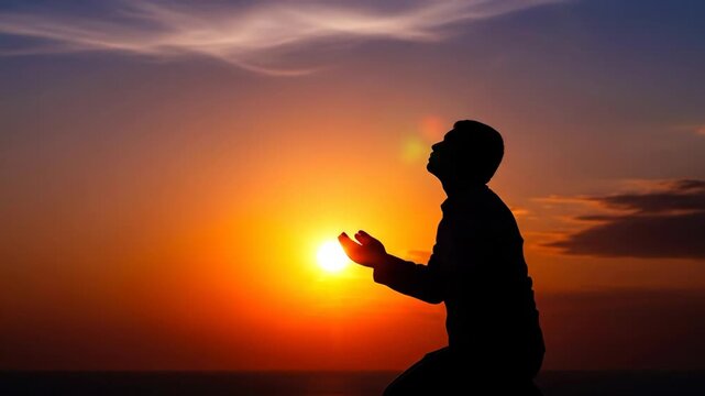 Man praying to God at sunset. Silhouette of believer kneeling while holding hands towards sky. Religious devotion, spiritual hope and worship in Catholic faith.