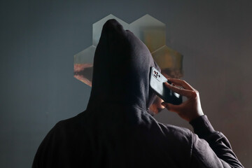 Anonymous man in black hoodie talking on smartphone indoors with his back to the camera, Phone Scammers, mysterious person using mobile phone. © eza