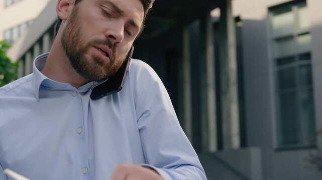 Serious Caucasian business man talk mobile phone writing notes city discussing project consulting client solving problem smartphone call male guy businessman plan strategy work idea notebook outdoor