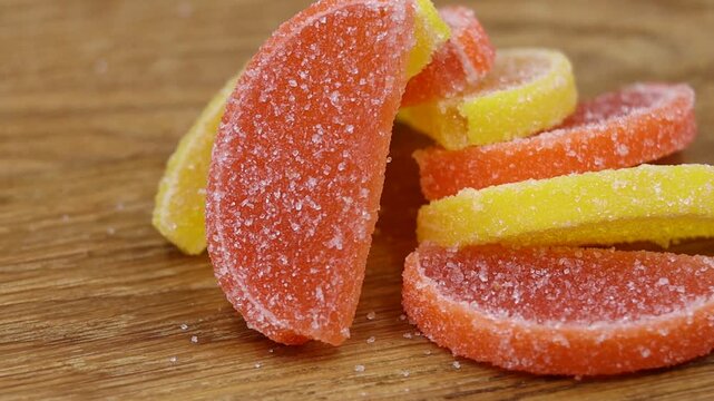 Close-up of sugar-coated lemon and orange jelly slices on a wooden table, rotating view.
