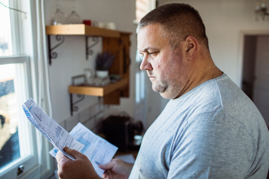 Worried man reading utility bills in kitchen
