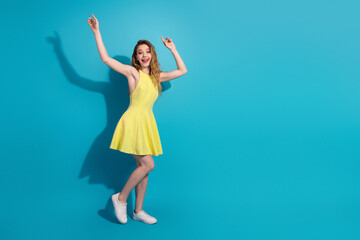 Excited young woman in a vibrant yellow dress posing against a bright blue background, radiating...
