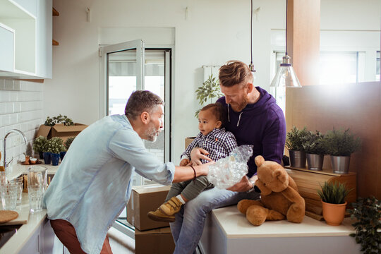 Two men unpacking with toddler in new home kitchen
