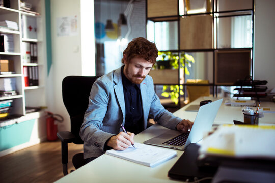 Young businessman writing notes at laptop in modern office