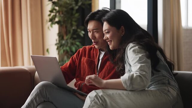 Smiling Asian couple choosing hotel on laptop, booking vacation tour, shopping
