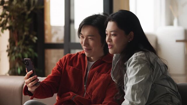 Cheerful Asian man and his girlfriend having video call on phone, communication