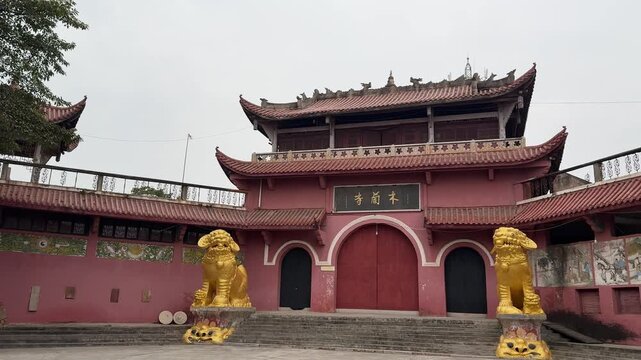 A smooth cinematic moving shot of the historic Mulan Temple in Xindu, Chengdu, featuring traditional red walls, a golden lion statue, and classic Chinese Buddhist architecture.