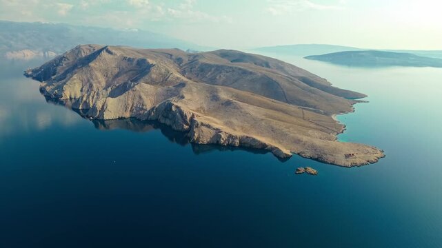 Elevated view of Prvić island with rugged cliffs and smooth hills rising from the Adriatic Sea. Minimalistic Mediterranean seascape highlighting isolation and coastal formations near Krk island