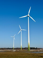 Three wind turbines standing in open field under bright blue sky.