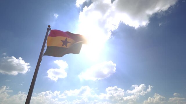 Ghana Flag waving on a Flagpole from a Moving Angle in front of a blue sky with clouds	