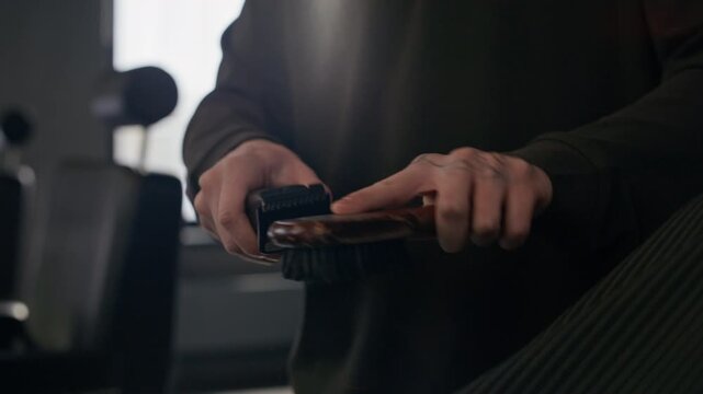 Close up of anonymous barber using brush to clean electric clipper after workday in barbershop