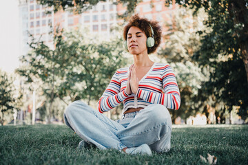Calm park moment a woman meditating wearing striped sweater headphones and jeans in a sunny city...