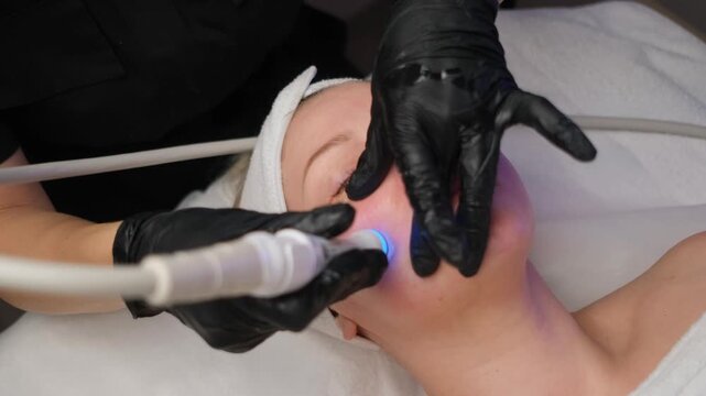 Cosmetologist performing a rejuvenating hydrafacial procedure with led therapy on a woman's cheek