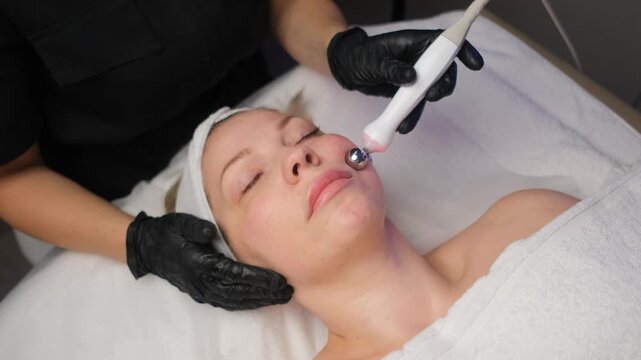 Professional cosmetologist performs a microcurrent facial toning procedure on a woman in a spa salon