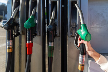 Hand Holding Green Fuel Pump Nozzle. Close-up of a hand holding a green fuel nozzle at a gas station, showing refueling equipment, energy supply, and transport service. © Iryna