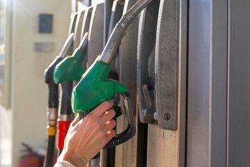 Hand Removing Green Gas Pump Nozzle. Close-up of a hand taking a green fuel nozzle from a gas station pump, showing refueling equipment, energy supply, and transport service. © Iryna