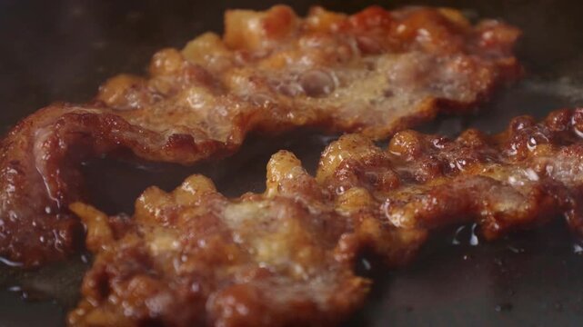 Slices of bacon frying in black pan closeup